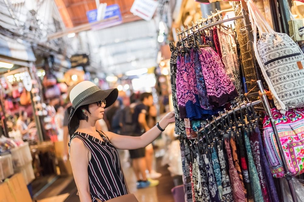 mujer con sombrero y gafas de sol mirando bolsos en bazar