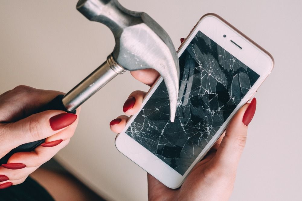 mano de mujer con martillo y movil con el cristal roto